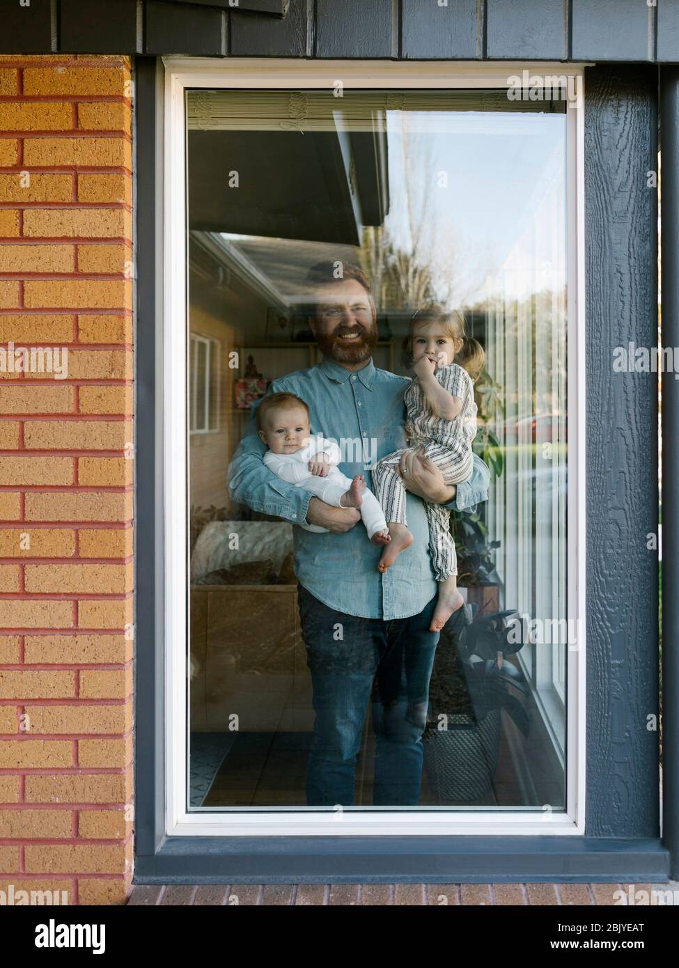Vater mit Kindern (2-5 Monate, 2-3) schaut durch das Fenster Stockfoto