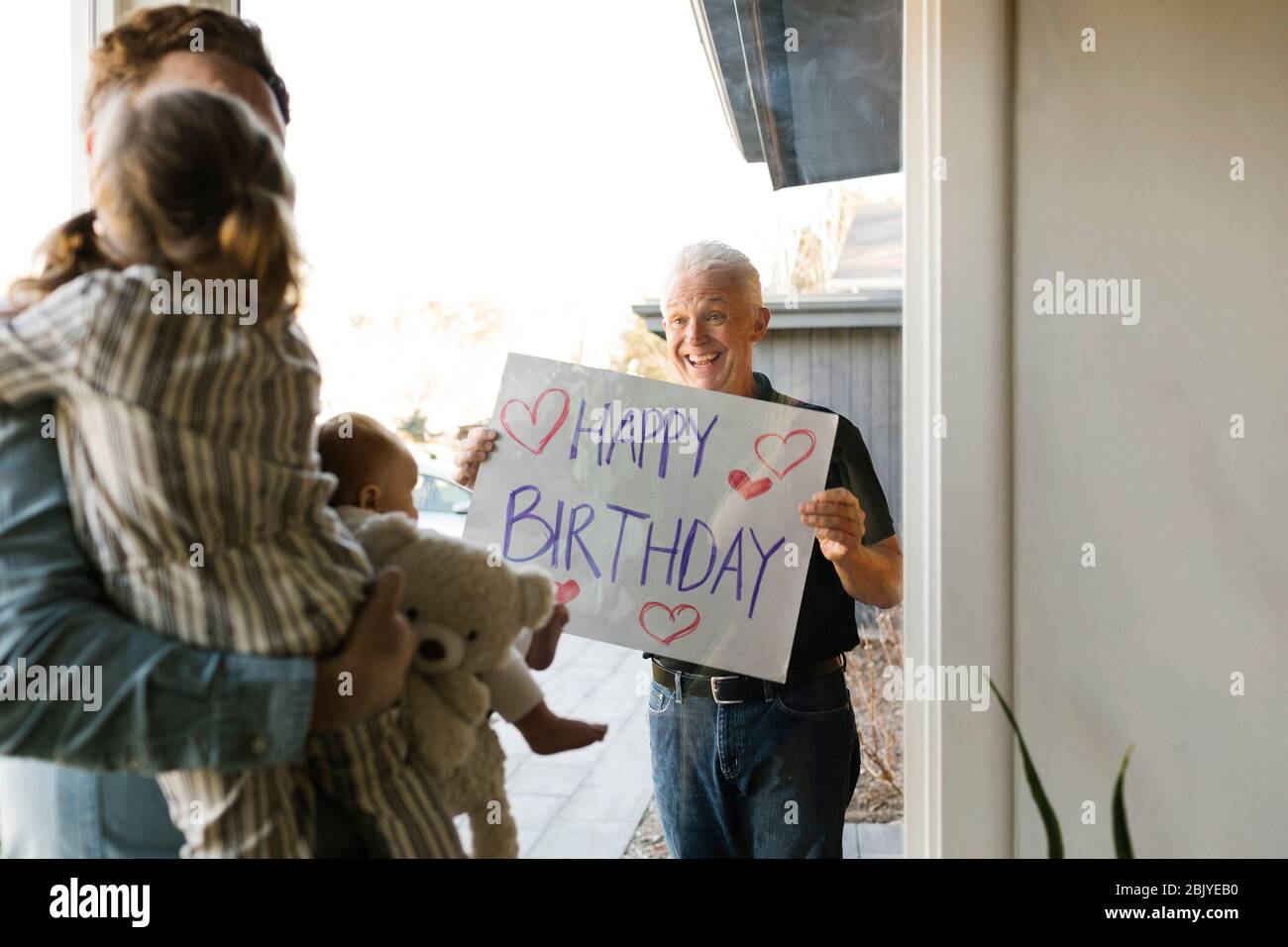 Großvater zeigt der Familie mit Enkelkindern (2-3 Monate, 2-3) durch das Fenster eine Glückwünsche zum Geburtstag Stockfoto