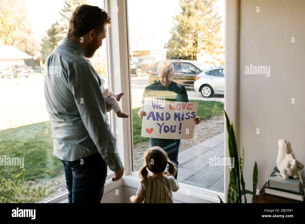 Großvater zeigt der Familie mit Enkelkindern (2-3 Monate, 2-3) durch das Fenster eine Nachricht Stockfoto