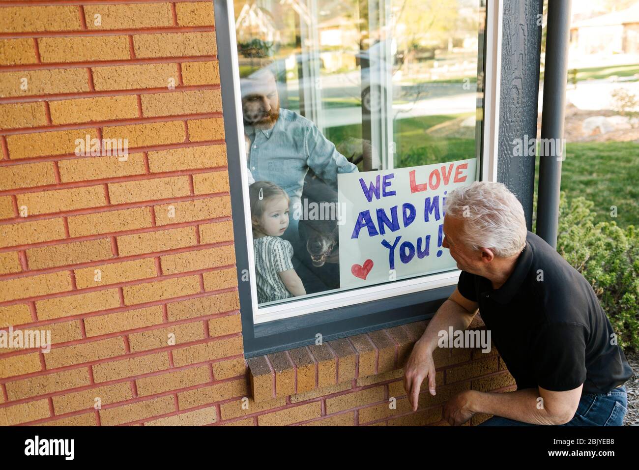 Großvater besucht Familie mit Enkelin (2-3) durch Fenster Stockfoto