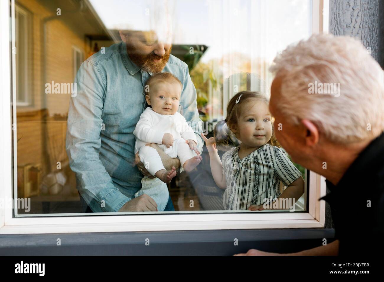 Großvater besucht Familie mit Enkeln (2-3 Monate, 2-3) durch Fenster Stockfoto