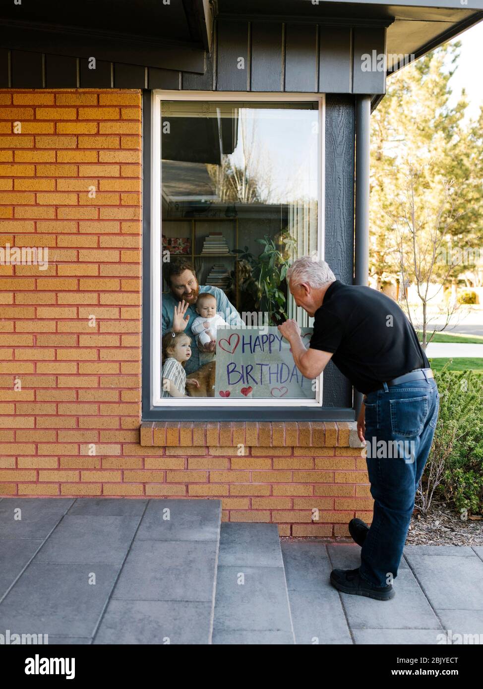 Großvater besucht Familie mit Enkeln (2-3 Monate, 2-3) durch Fenster Stockfoto