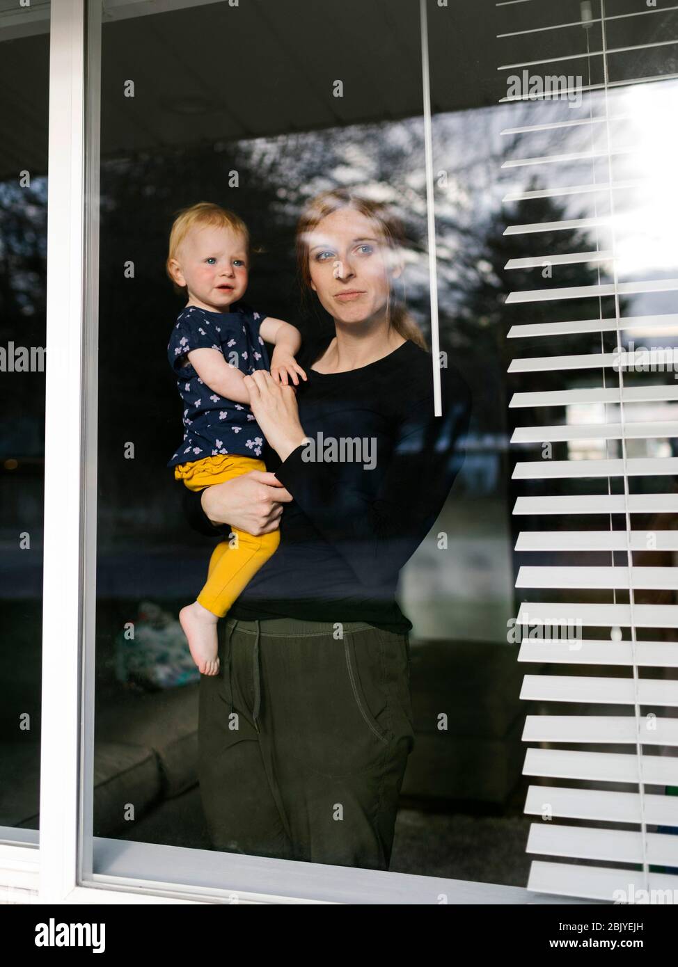 Mutter hält Tochter (2-3) und schaut durch das Fenster Stockfoto