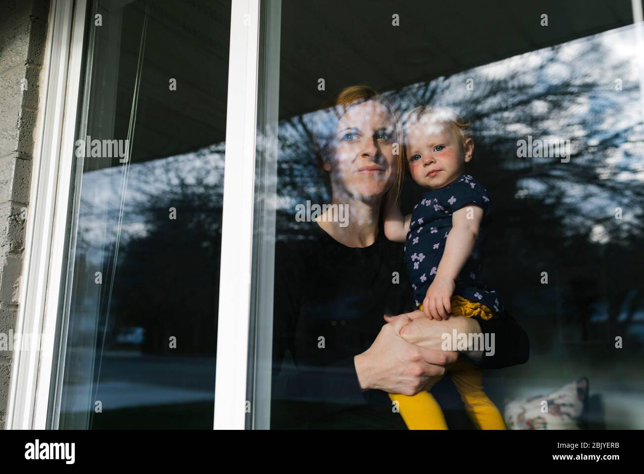 Mutter hält Tochter (2-3) und schaut durch das Fenster Stockfoto