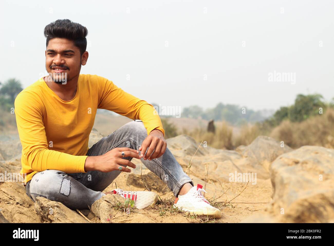 Junger Mann Modell sitzt in der Nähe eines Flusses Strand trägt T-Shirt und Jeans Stockfoto