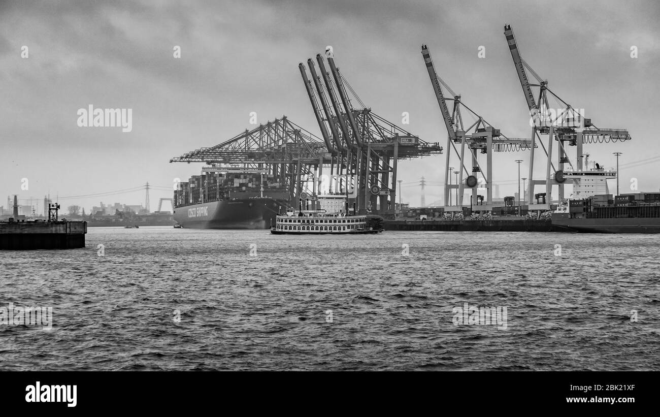 Hamburger Containerhafen mit einigen Schiffen, die Container zu den Frachtern mit dramatischem Himmel/Wolken transportieren, Deutschland Stockfoto