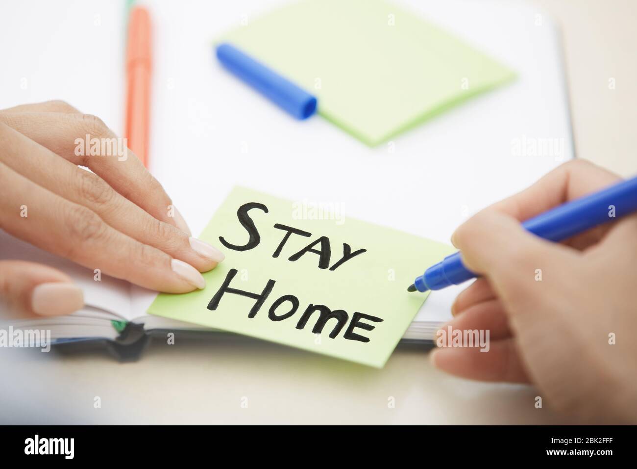 Hände von Frau schreiben auf Haftnotiz mit Stay Home Text Stockfoto