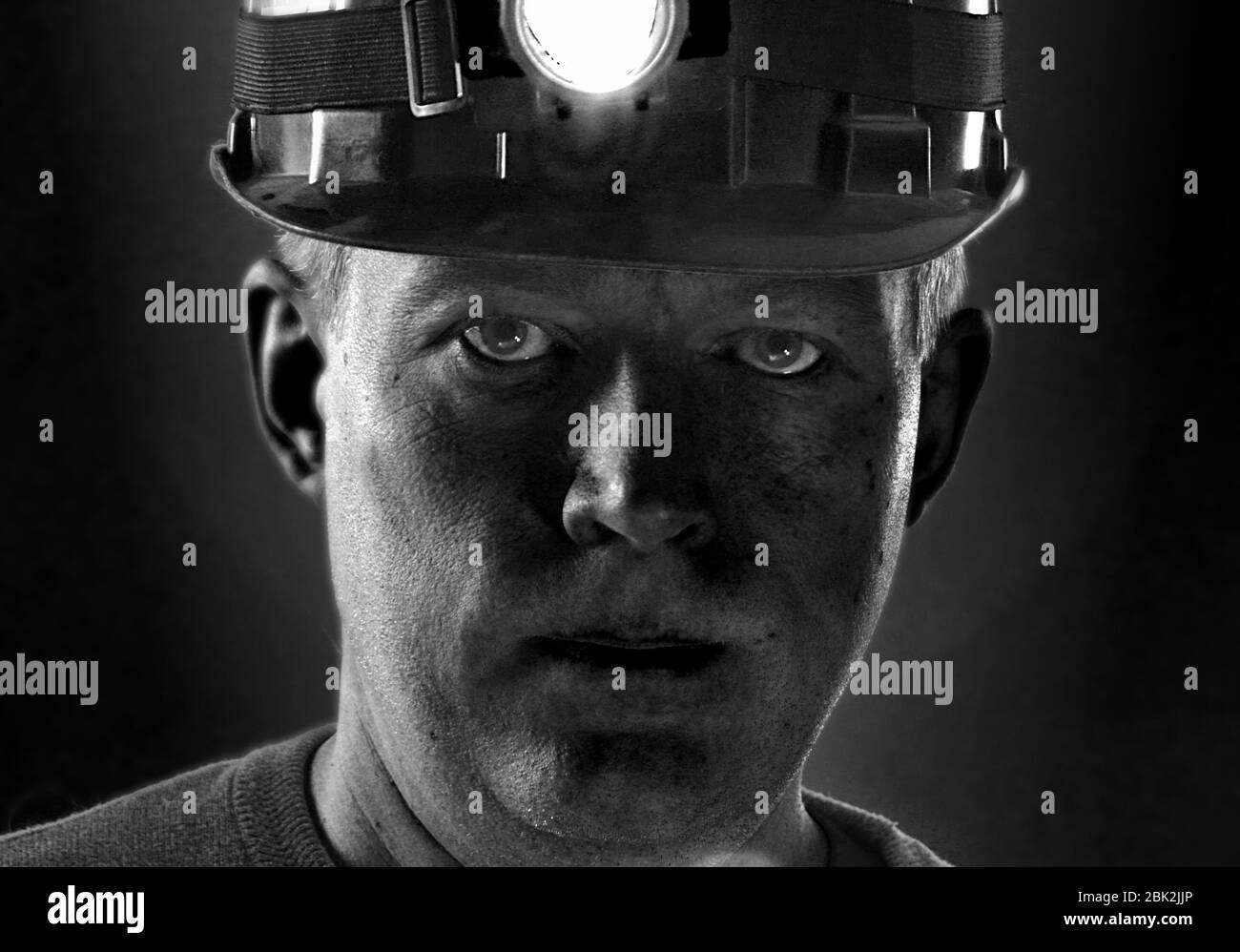 Schmutziges Gesicht des Kohlemeiters im Helm mit Licht. Porträt des Minenarbeiters. Mann müde von harter Arbeit. Stockfoto