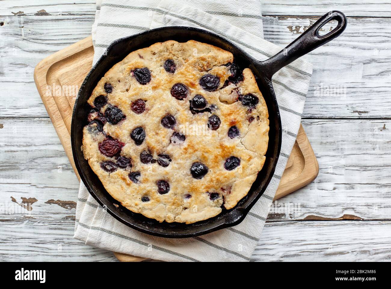 Frisch zubereitetes, hausgemachtes Kirschpflaster, das in einer gusseisernen Pfanne auf einem rustikalen Tisch aus weißem Holz gebacken wird. Bild von oben aufgenommen. Stockfoto