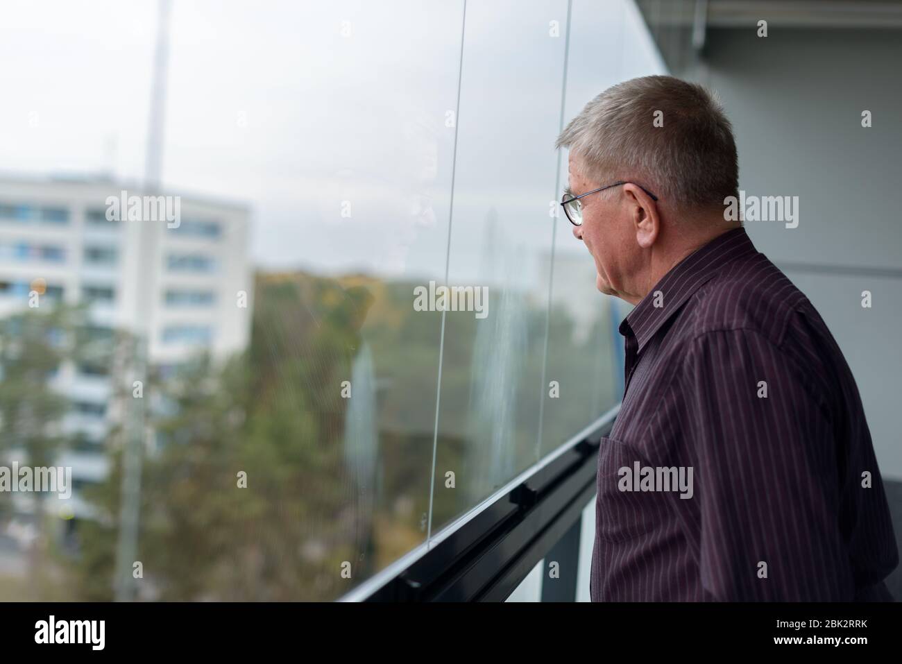 Der alte Mann denkt nach, während er aus dem Glasfenster des modernen Gebäudes schaut Stockfoto
