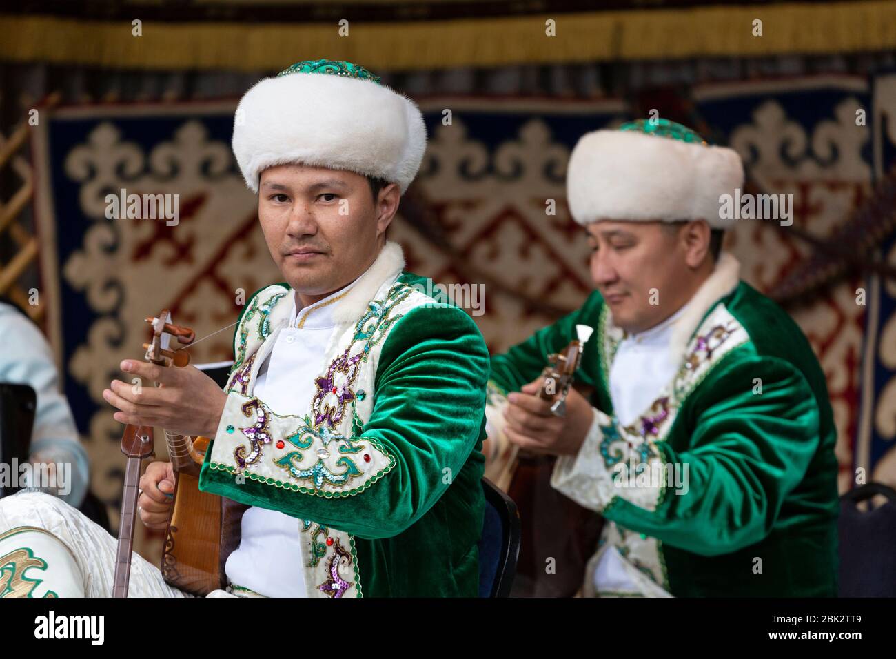 Porträt zweier Männer in traditioneller Kleidung, die eine Dombra auf einer Bühne beim Kasachstan-Frühlingsfest in Victoria Embankment Gardens, London spielen Stockfoto