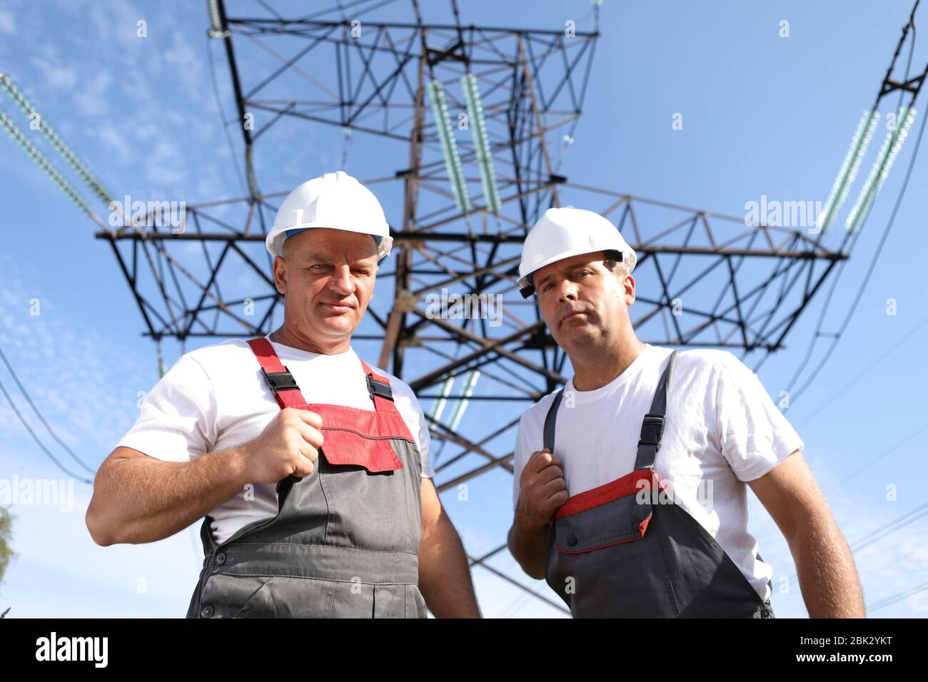 Zwei Erwachsene männliche Elektriker zeigen wie. Zwei Arbeiter von Kraftwerken auf dem Hintergrund eines elektrischen Pylons. Elektrische Unterstützung 8000 Kilowatt Stockfoto