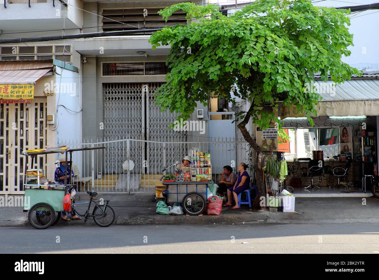 Zwei Hausdle auf Bürgersteig unter Ast von Baum am Mittag, vietnamesische Frau Straßenverkäufer verkaufen Essen und Trinken mit Handwagen auf der städtischen Straße, Vietnam Stockfoto
