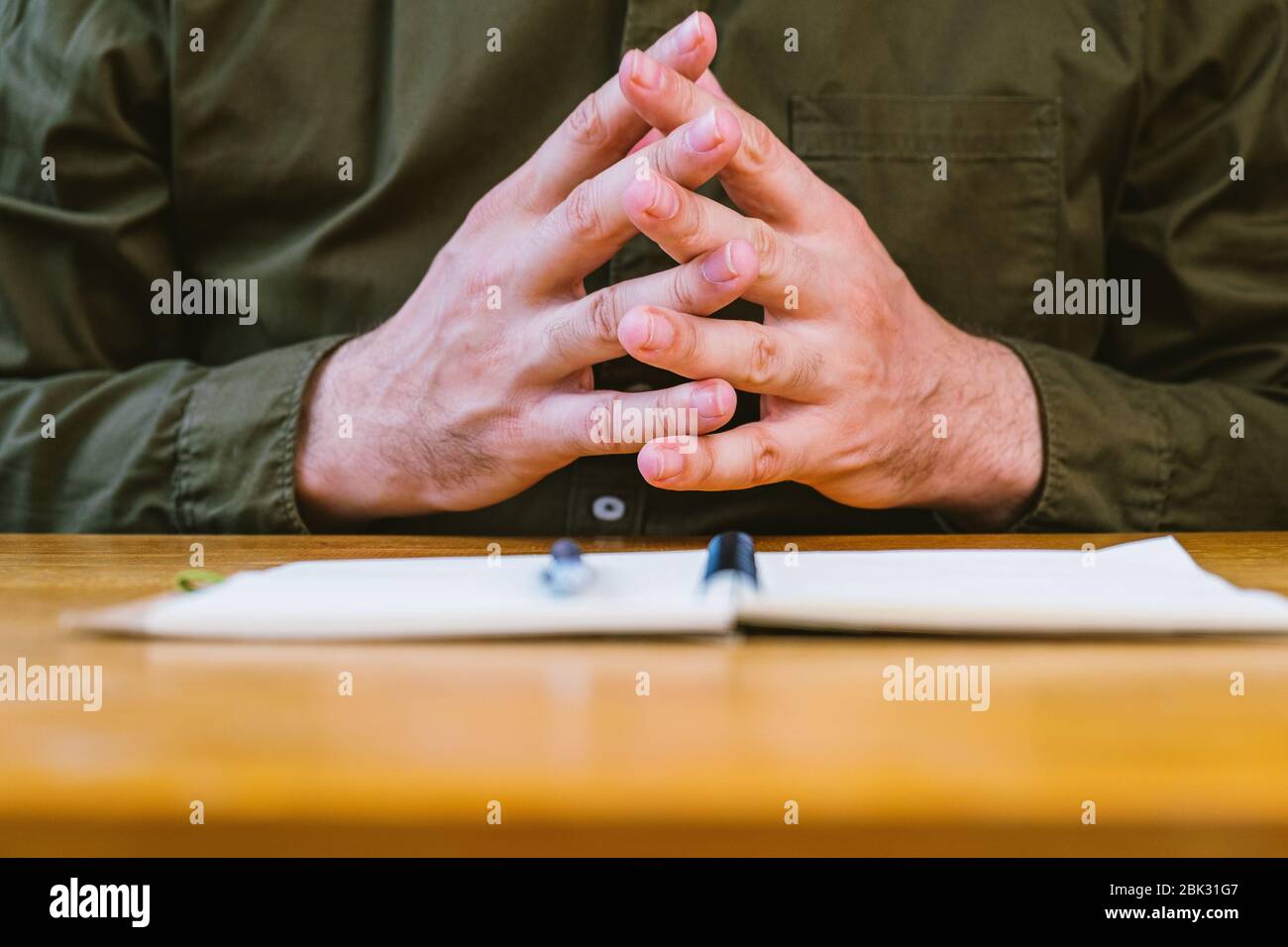 Geschäftsmann hält Arme auf Notebook im Büro während der Sitzung, Finger verflochten, Detail, flache Schulden des Feldes Stockfoto