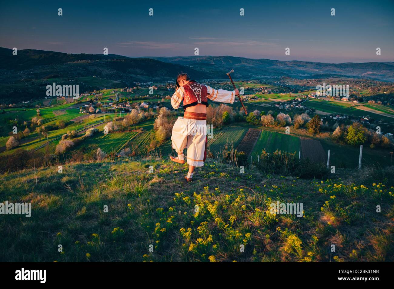 Junger Mann in Tracht tanzt in der Frühlingsnatur bei Sonnenaufgang. Bearbeiten Sie den Bereich. Schöne Frühlingslandschaft im Hintergrund. Hrinova Dorf in der Slowakei Stockfoto