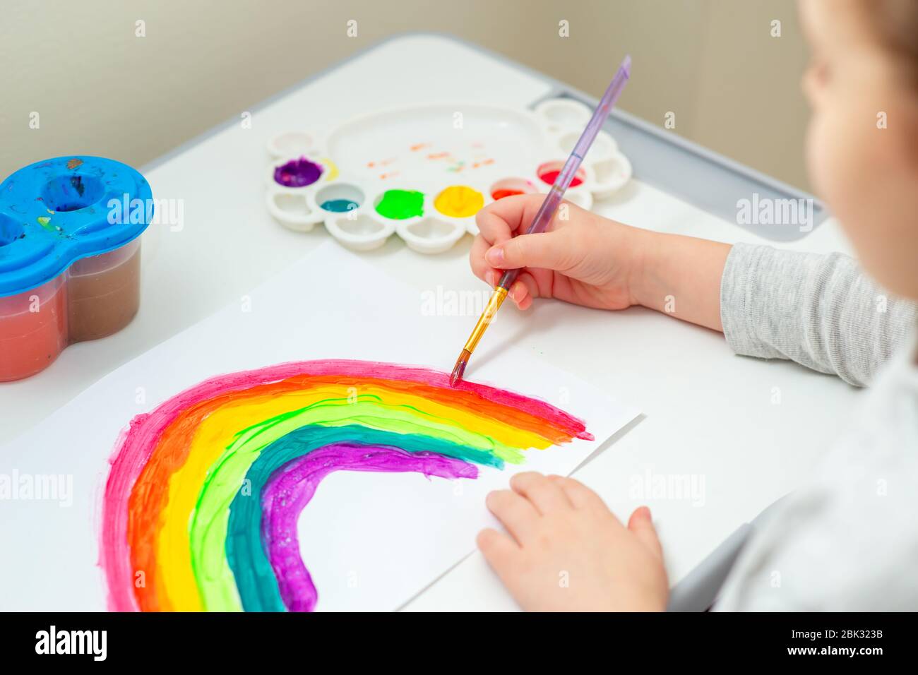 Kind zeichnet Regenbogen mit Aquarellen auf dem Blatt Papier. Kreativitätskonzept. Stockfoto