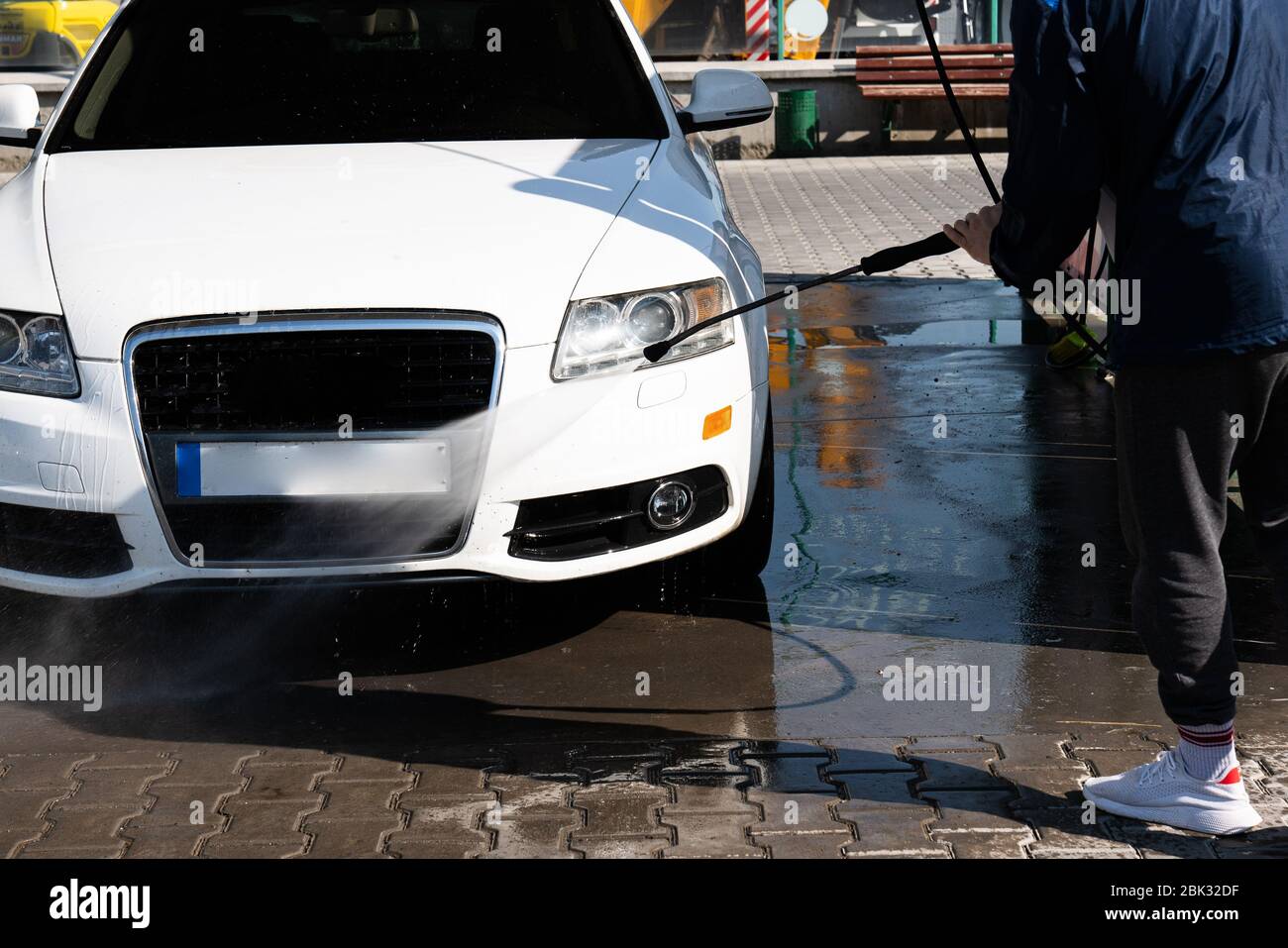 Aufnahme eines lässigen Mannes, der sein Auto unter Hochdruckwasser im Freien wäscht. Stockfoto