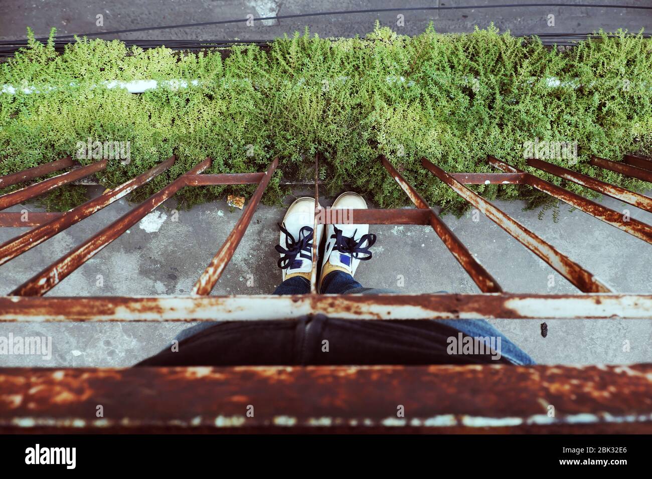 Frau stehen nestle nahe Rost Handlauf Balkon in Stress und Angst durch Gewalt, Stillstand im Leben, Draufsicht Fuß tragen Jeans und Schuhe mit Gras o Stockfoto