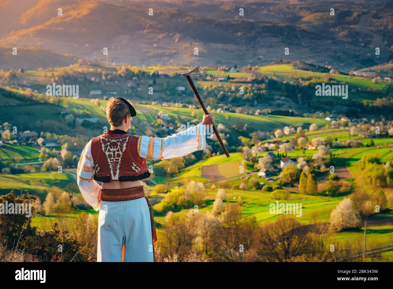 Ein junger Mann in slowakischer Tracht blickt auf die Frühlingslandschaft im Dorf Hrinova in der Slowakei. Aufgehende Sonne und Frühling blühende Bäume in der Stockfoto