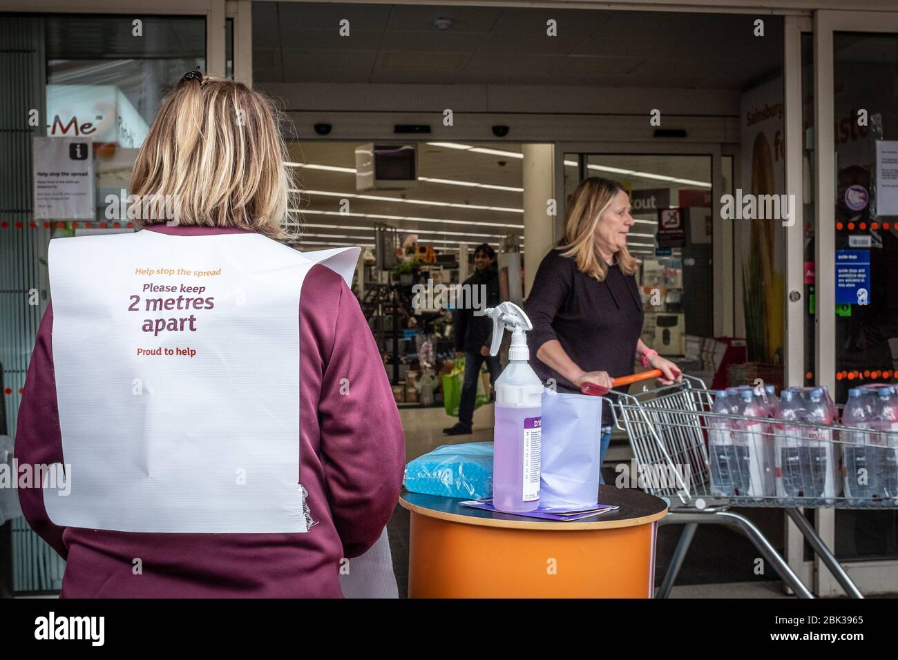 Mitarbeiter im Sainsbury's Supermarkt in England, Großbritannien steht vor dem Eingang mit Reinigungs- und Desinfektionsmitteln während der COVID-Pandemie Stockfoto