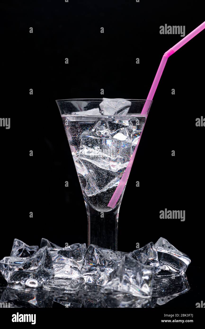 Klares Trinkglas mit Eis und einem rosa Plastikstroh, umgeben von Eiswürfeln Stockfoto