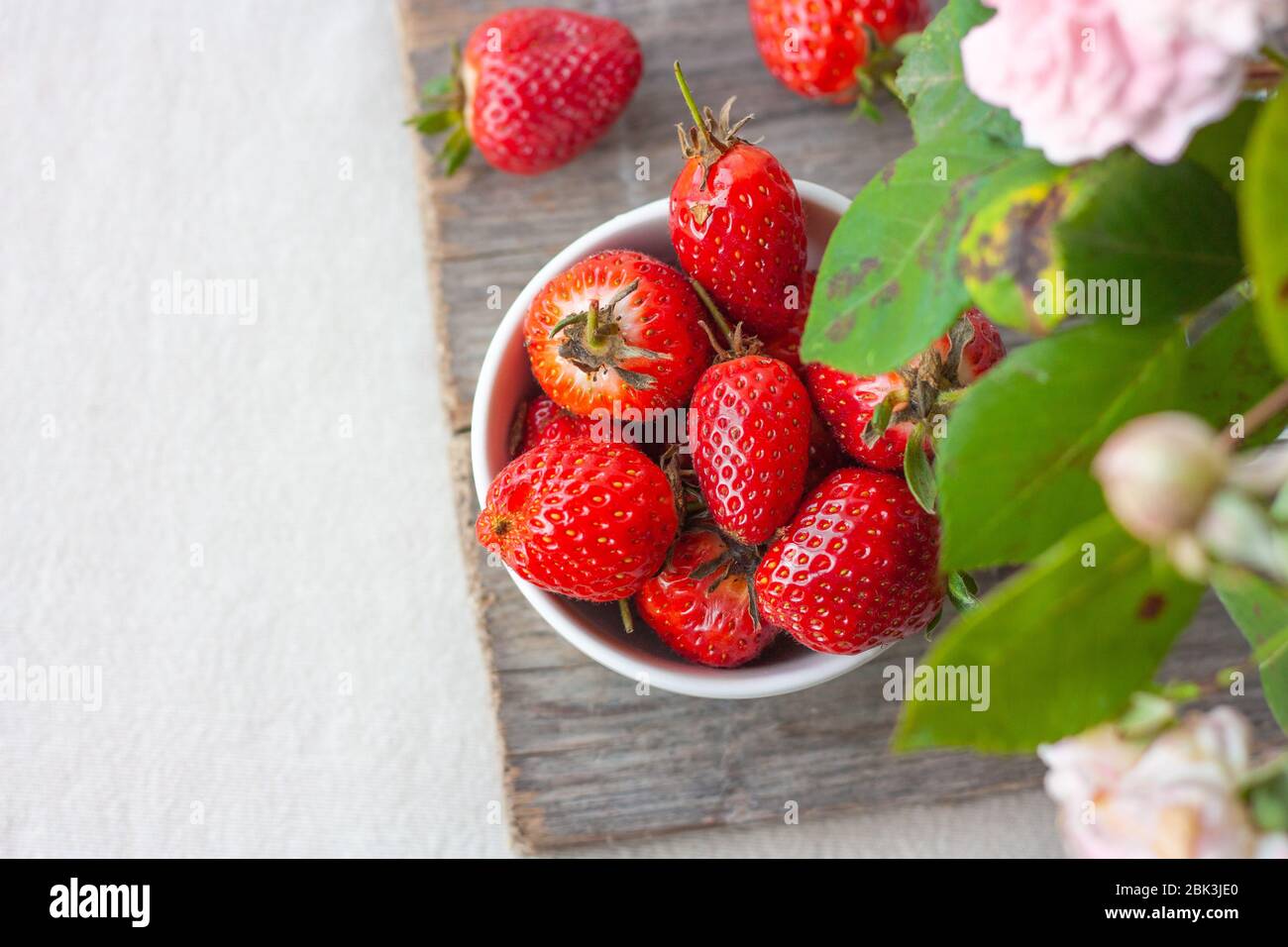 Obstschale voll mit frischen, roten, juckigen Erdbeeren auf Holztisch. Pastellfarbene Dekoration mit Blumenarrangement und Platz für Text. Draufsicht. Stockfoto