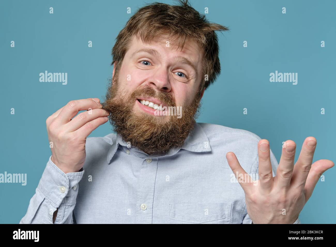 Der Mann ist unzufrieden mit seinem zotteligen Haar und Bart, er braucht dringend eine Friseurladen. Konzept der Quarantäne während einer Virusepidemie. Stockfoto