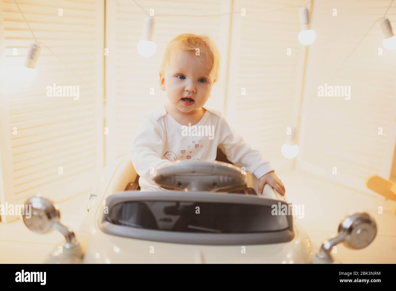 Kleiner blonder Junge auf einem beigen Retro-Spielzeugauto.kleiner blonder Junge auf einem beigen Retro-Spielzeugauto. Stockfoto