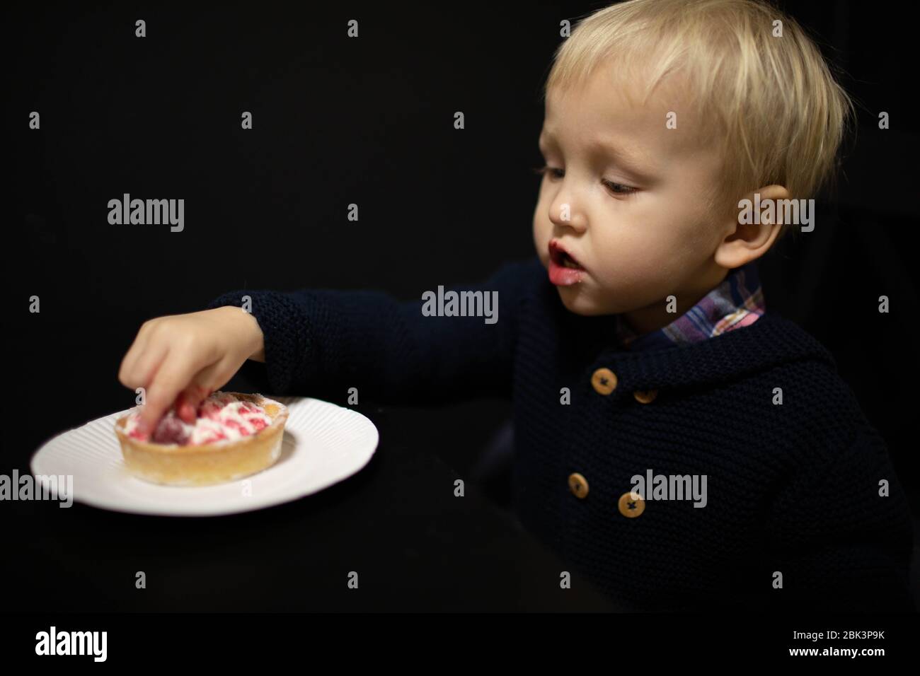 Ein kleiner blonder Junge isst Süßigkeiten. Köstliches Tartlet. Stockfoto