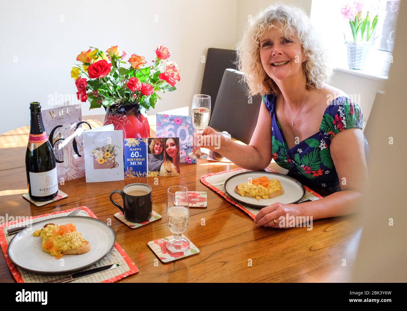 Frau zu Hause genießt ihr 60. Geburtstag Frühstück mit Rührei mit geräuchertem Lachs und Sekt während Coronavirus Lockdown UK Stockfoto