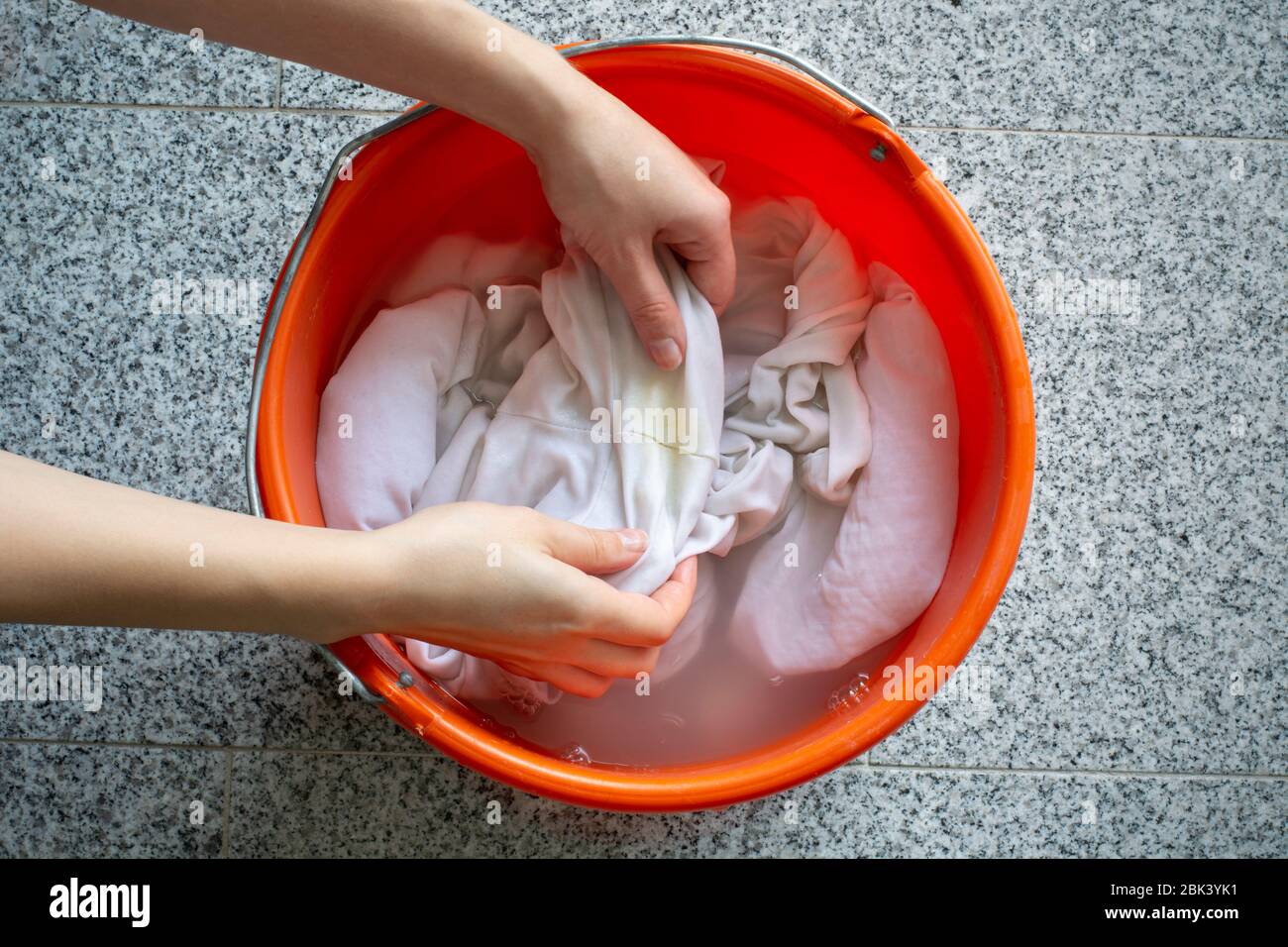 Reinigung der Wäsche manuell. Damenhände waschen schmutzige weiße Hemden mit gelben Schweißflecken, um sie in einem Eimer zu tränken Stockfoto