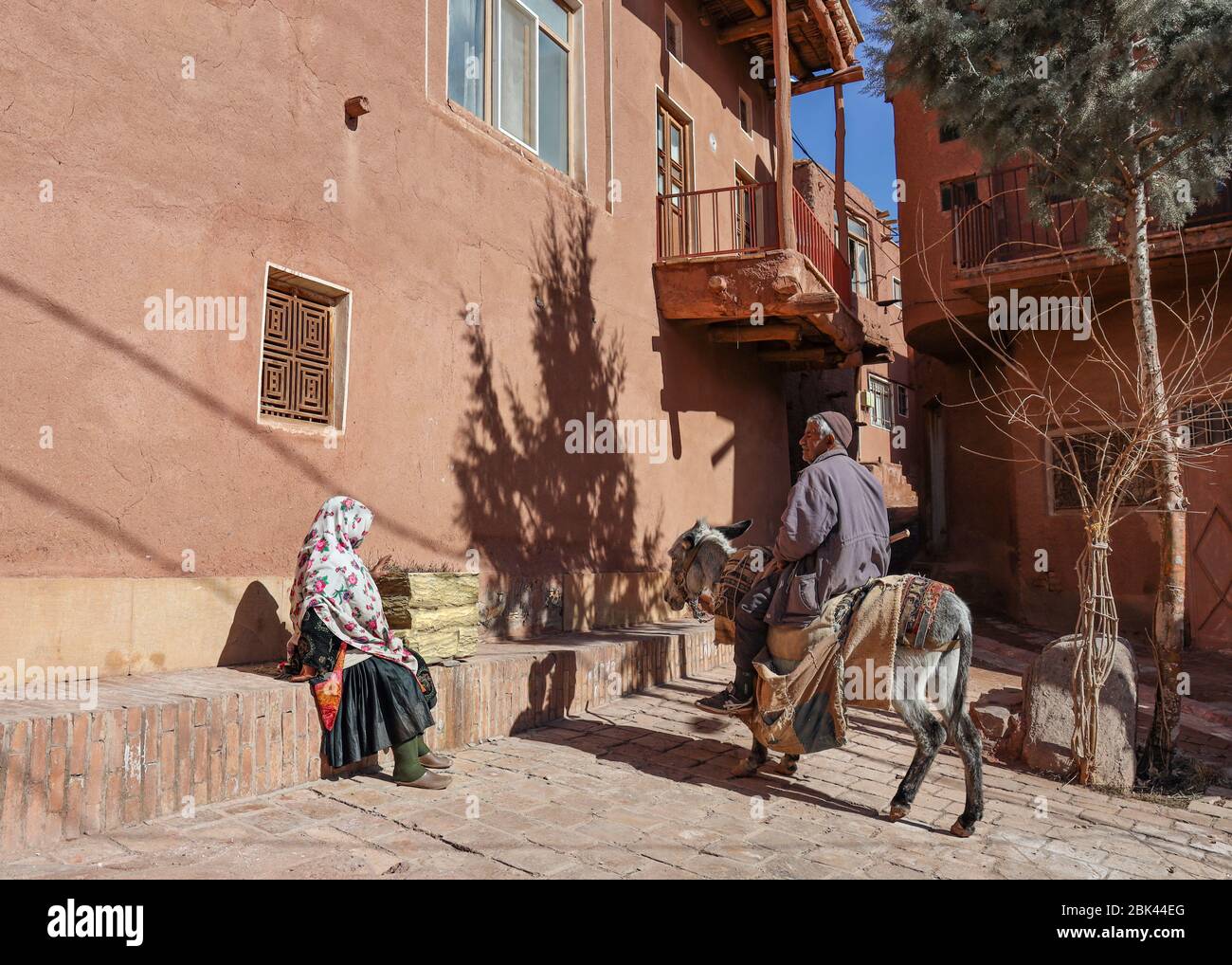 Ein alter Mann sitzt auf einem Esel und spricht mit einer Frau in traditioneller Kleidung im Dorf Abyaneh, Provinz Esfahan, Iran, Persien, Naher Osten Stockfoto