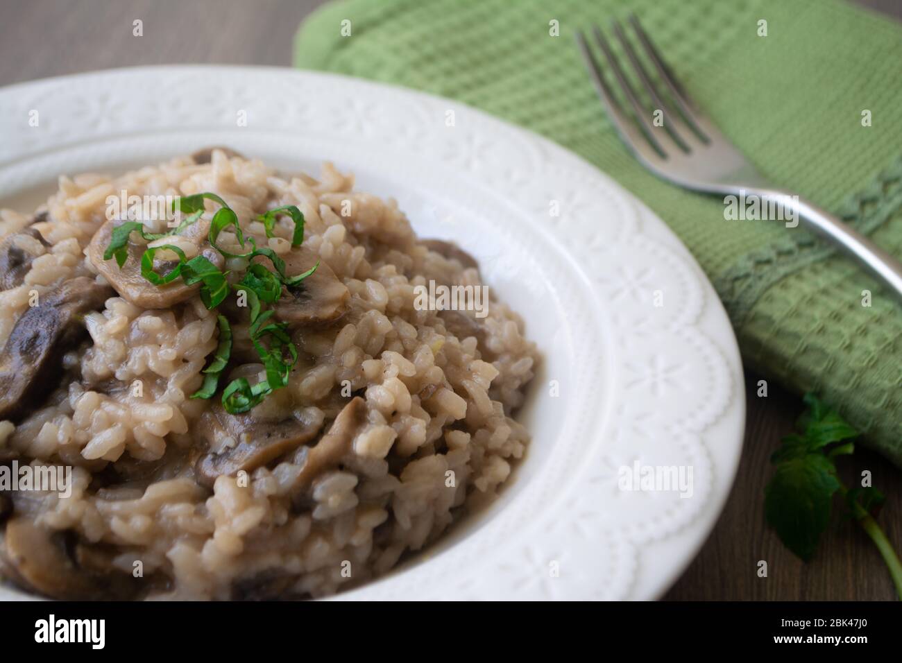 Klassisches italienisches veganes Pilzrisotto mit arborio Reis, Pilzen, Zwiebeln und Knoblauch, garniert mit Basilikumbändchen auf einer rustikalen Holzoberfläche mit viel Geschmack Stockfoto