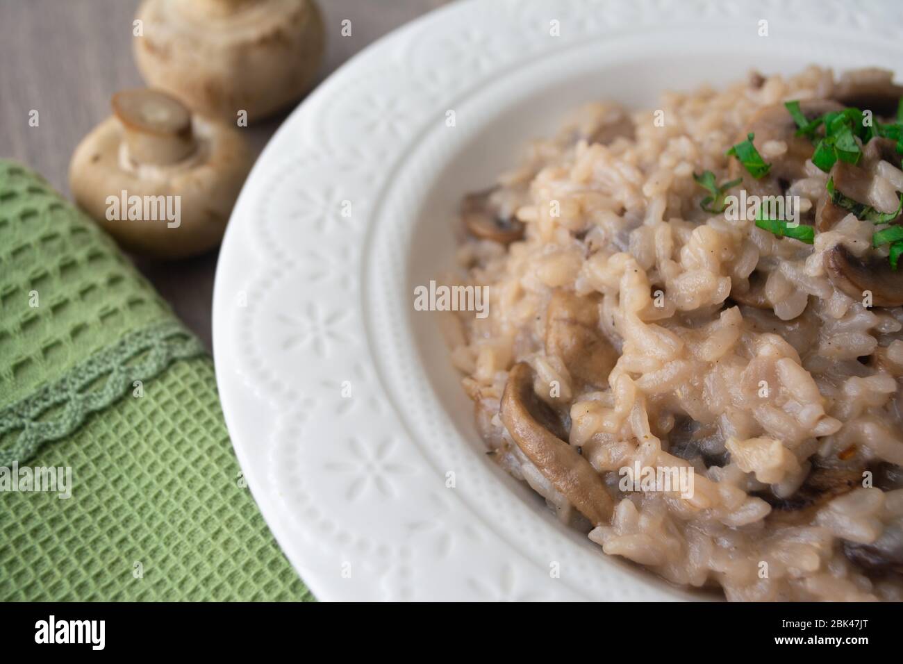 Klassisches italienisches veganes Pilzrisotto mit arborio Reis, Pilzen, Zwiebeln und Knoblauch, garniert mit Basilikumbändchen auf einer rustikalen Holzoberfläche mit viel Geschmack Stockfoto