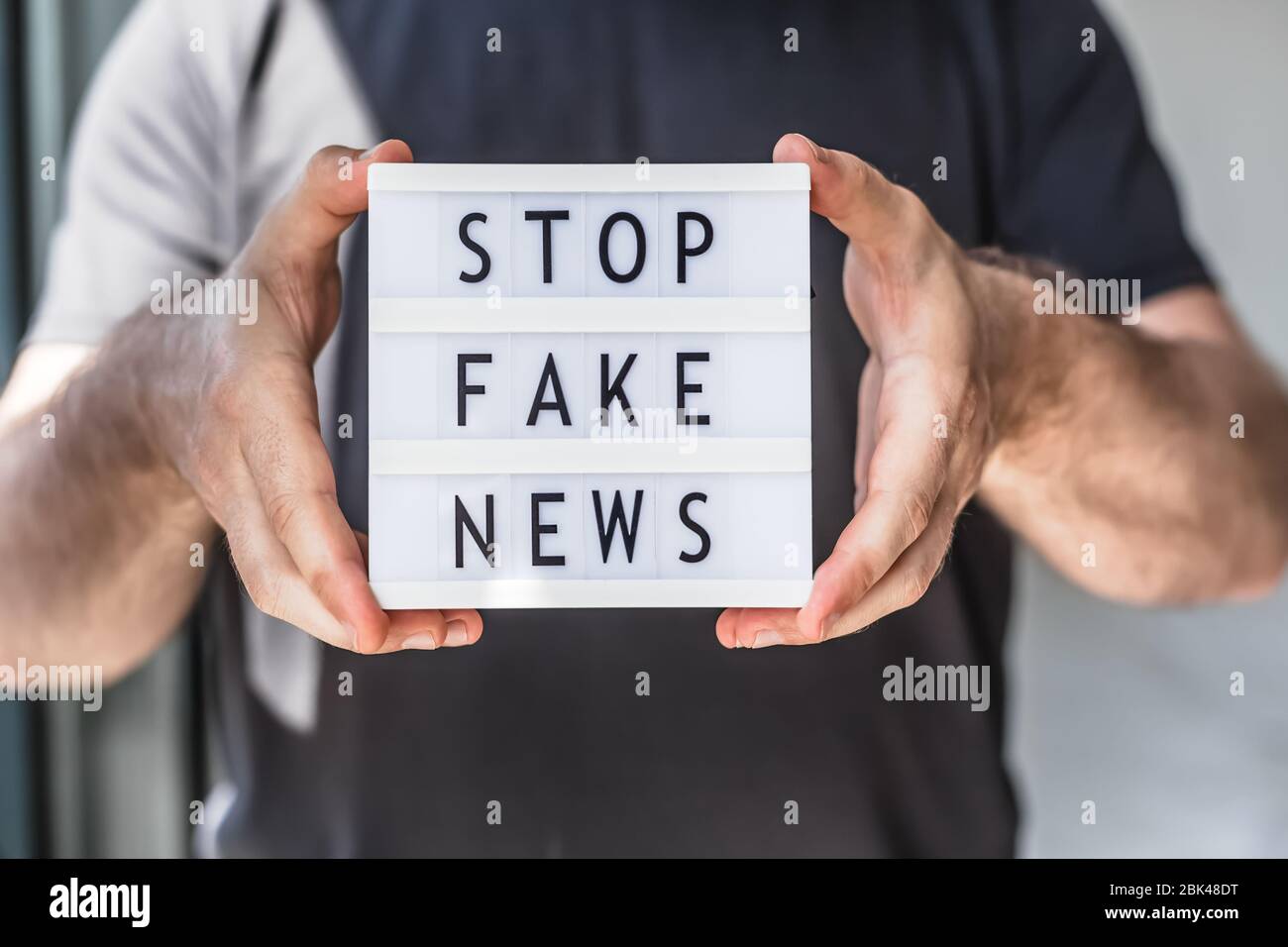 Fake News Infosemics during Covid-19 Pandemie Concept. Mann Hände halten Leuchtkasten mit Text Stoppen Fake News im Vordergrund. Die Leute wollen den Trut kennen Stockfoto