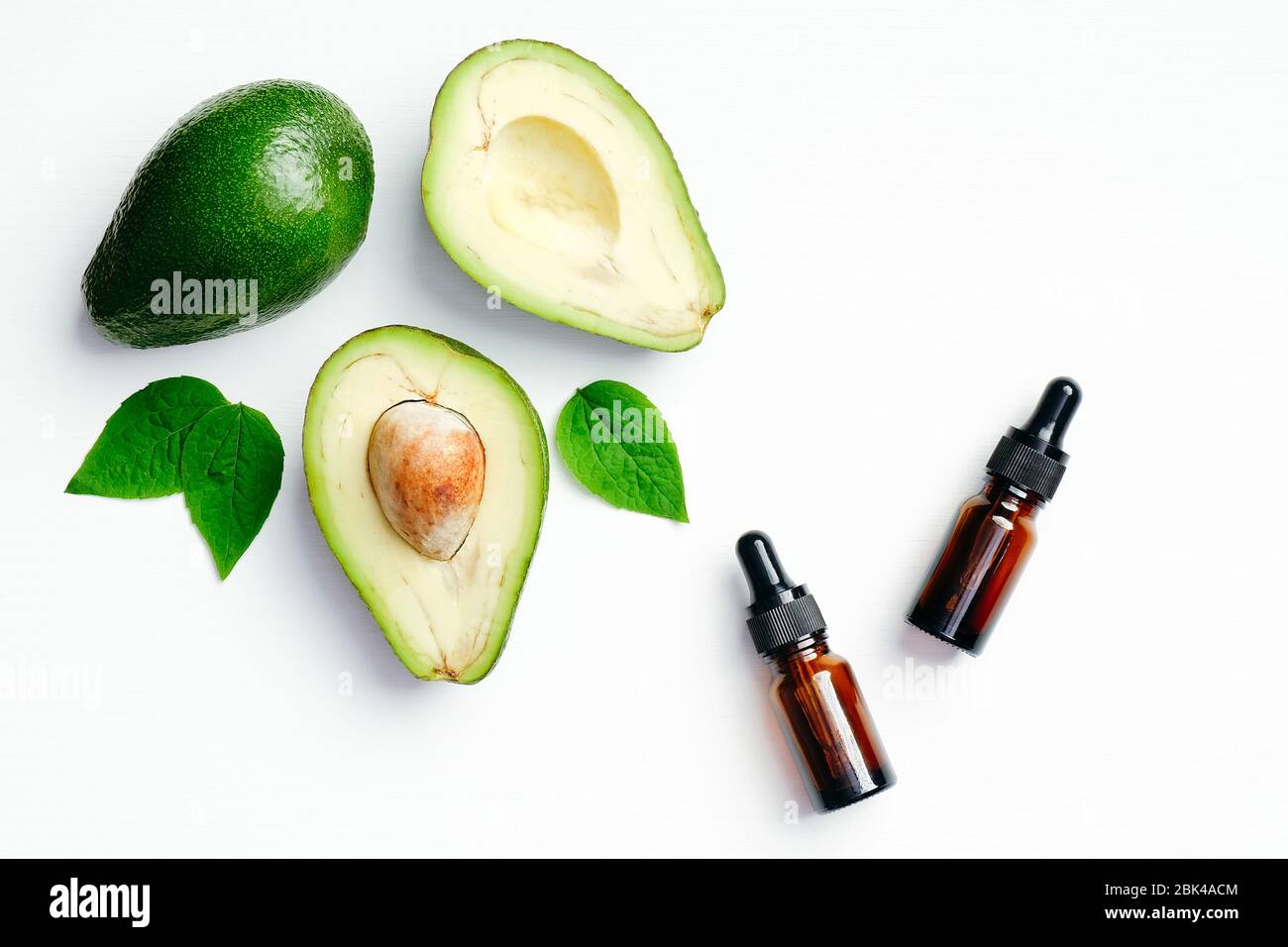 Flaschen mit ätherischen Ölen und Avocado mit grünen Blättern auf weißem Hintergrund. Flach liegend, Draufsicht. Aromatherapie Massage Öl, Avocado Behandlung Konzept Stockfoto