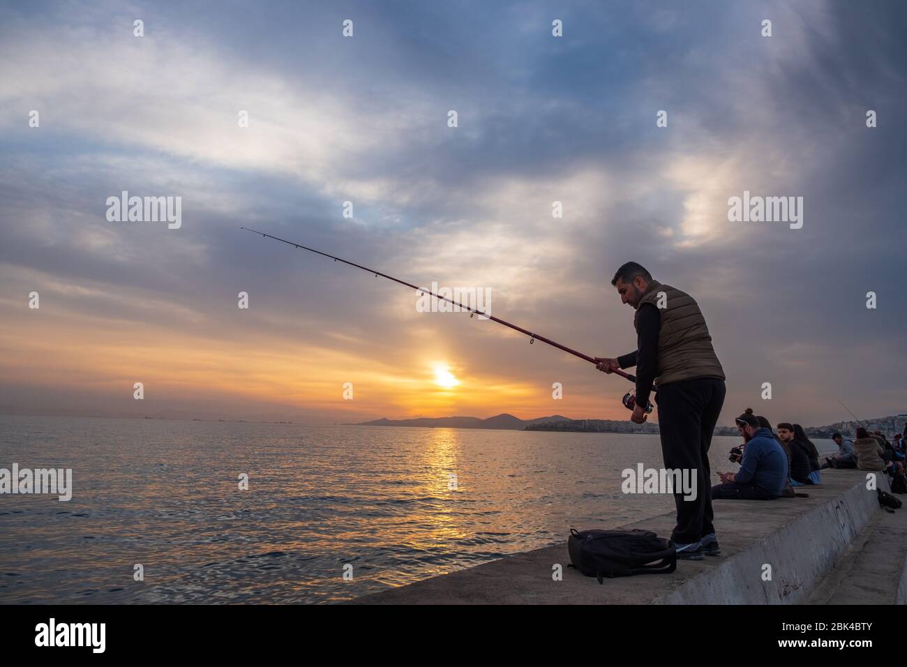 Athen, Griechenland - 11. März 2019: Wunderschöne Sonnenuntergangsszene eines Fischers und anderer Menschen, die sich an der Küste von Palaio Faliro in Athen amüsieren Stockfoto