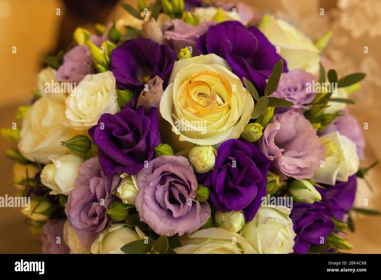 Goldene Trauringe auf einem Hochzeitsstrauß aus gelben und lila Rosen. Nahaufnahme. Hochzeit. Stockfoto