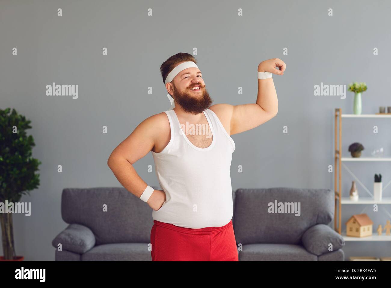 Lustiger fetter Mann in roten Shorts und weißem T-Shirt lächelnd Übungen im Raum machen Stockfoto