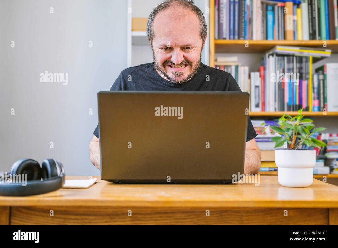 Mann, der vom Home Office aus arbeitete, machte einen Fehler, Gesichtsausdruck. Bärtiger Mann hinter Vintage Schreibtisch zu Hause saß etwas falsch gemacht und mit Geschäft Stockfoto