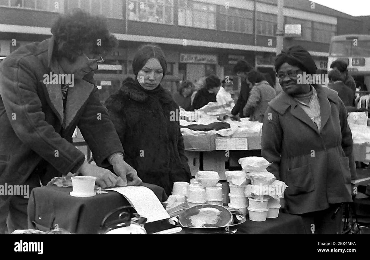 Kunden schauen sich 1974 einen Stand im Freien auf dem Longsight Market, Dickenson Road, Manchester, England, großbritannien, an. Stockfoto