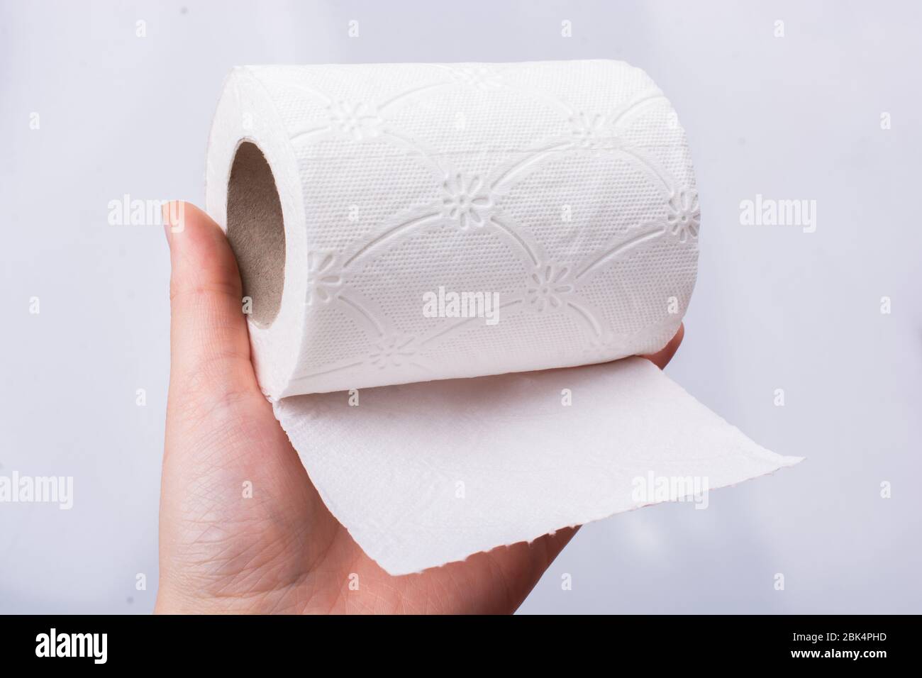 Eine weibliche Hand nimmt eine Rolle weißes Toilettenpapier in die Hand. Stockfoto