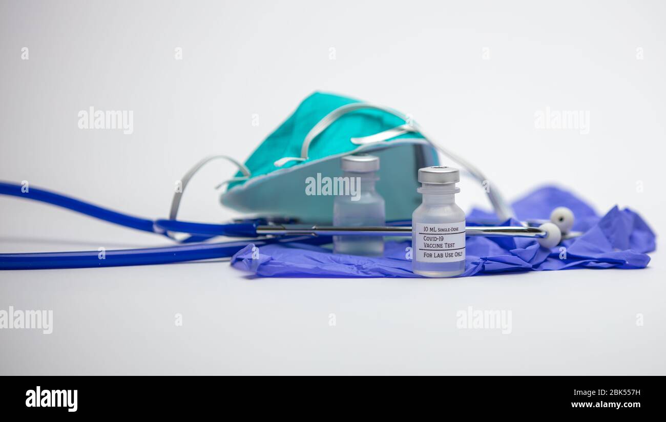 Covid-19 Impfstoff-Testfläschchen auf medizinischen Gummihandschuhen mit Stethoskop und Atemschutzmaske im Hintergrund. Stockfoto