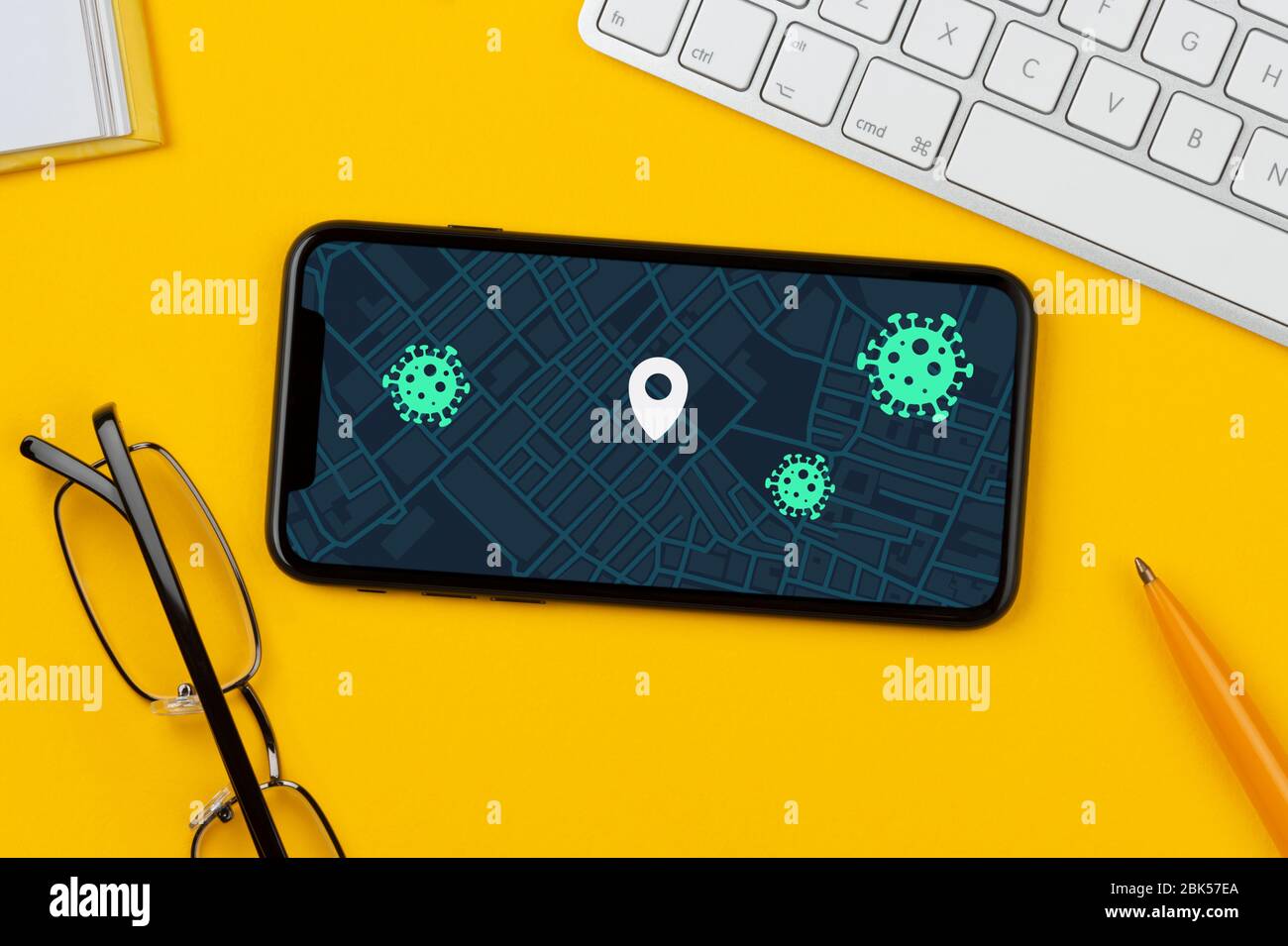 Ein Smartphone, das eine fiktive Covid-19-App zur Kontaktverfolgung zeigt, ruht auf einem gelben Hintergrund zusammen mit Tastatur, Brille, Stift und Buch. Stockfoto
