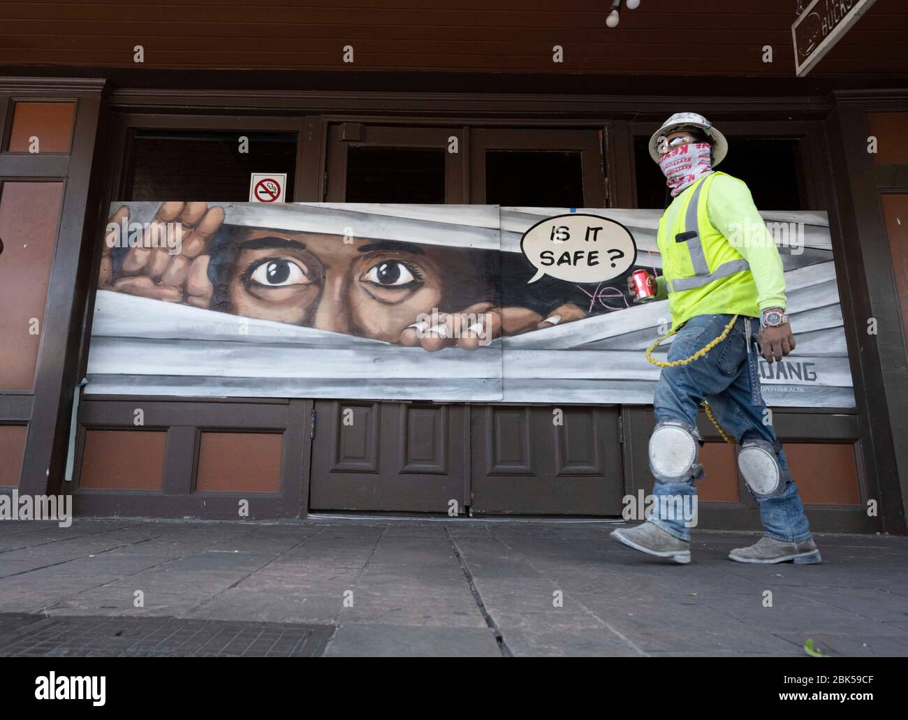 Bauarbeiter, die eine Gesichtsmaske tragen, gehen vor bunten Wandmalereien, die vernagelten Bar- und Restaurantfronten im normalerweise belebten Unterhaltungsviertel Sixth Street schmücken. In Austin, Texas, sechs Wochen nach einer Betriebsruhe aufgrund der Coronavirus-Pandemie. Stockfoto