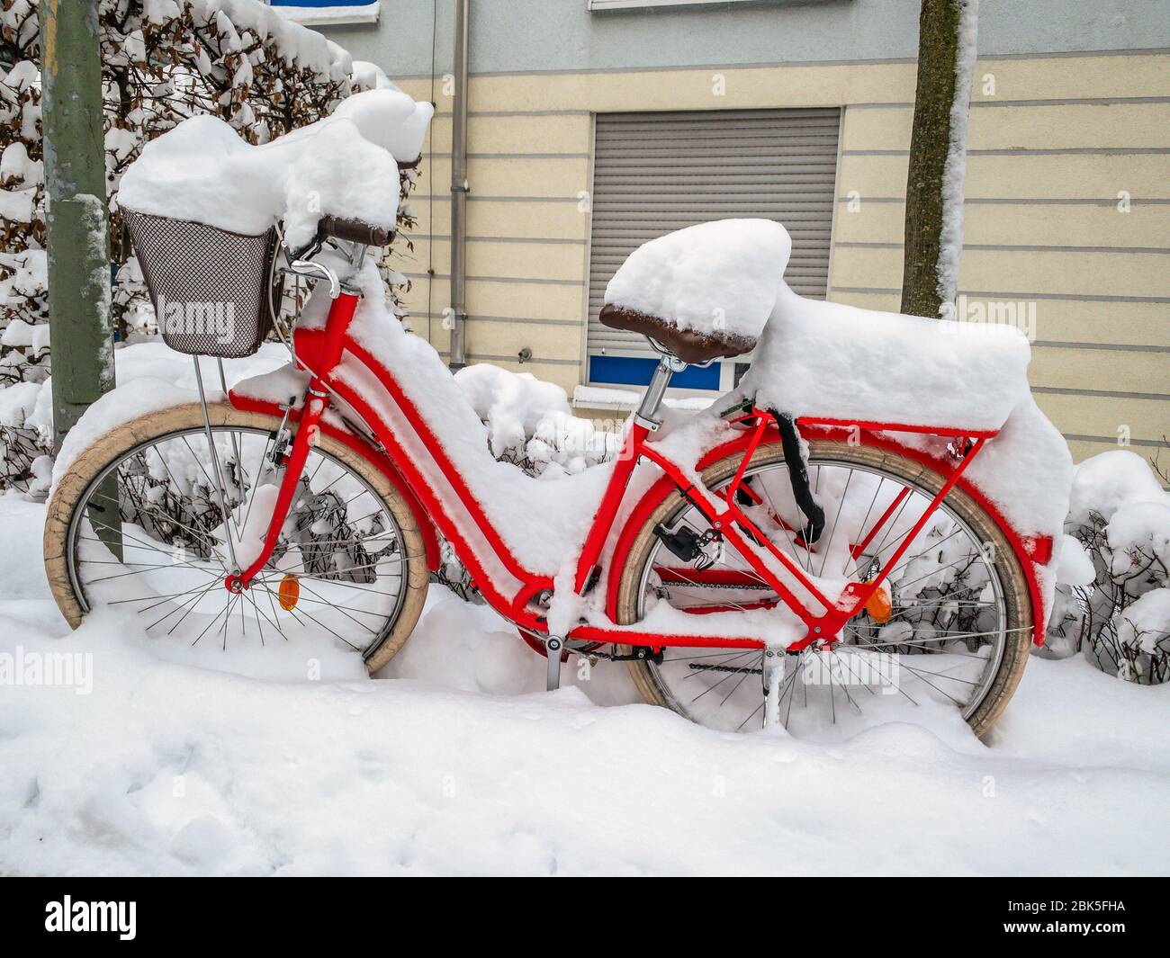 Ein buntes rotes Fahrrad mit vielen Neuschnee vor einer Hausfassade. Stockfoto
