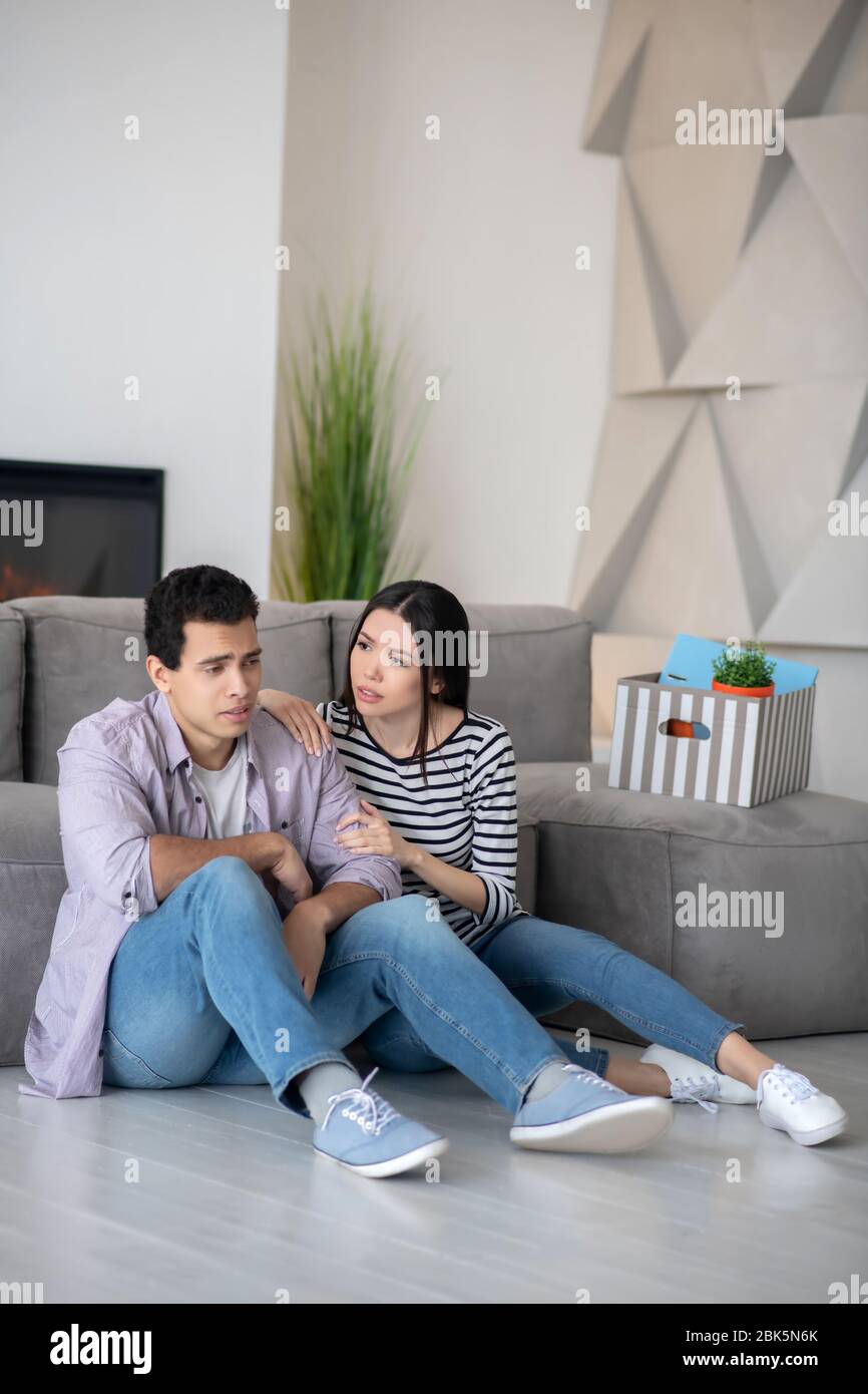 Der junge traurige Mann und die fürsorgliche Frau sitzen auf dem Boden. Stockfoto