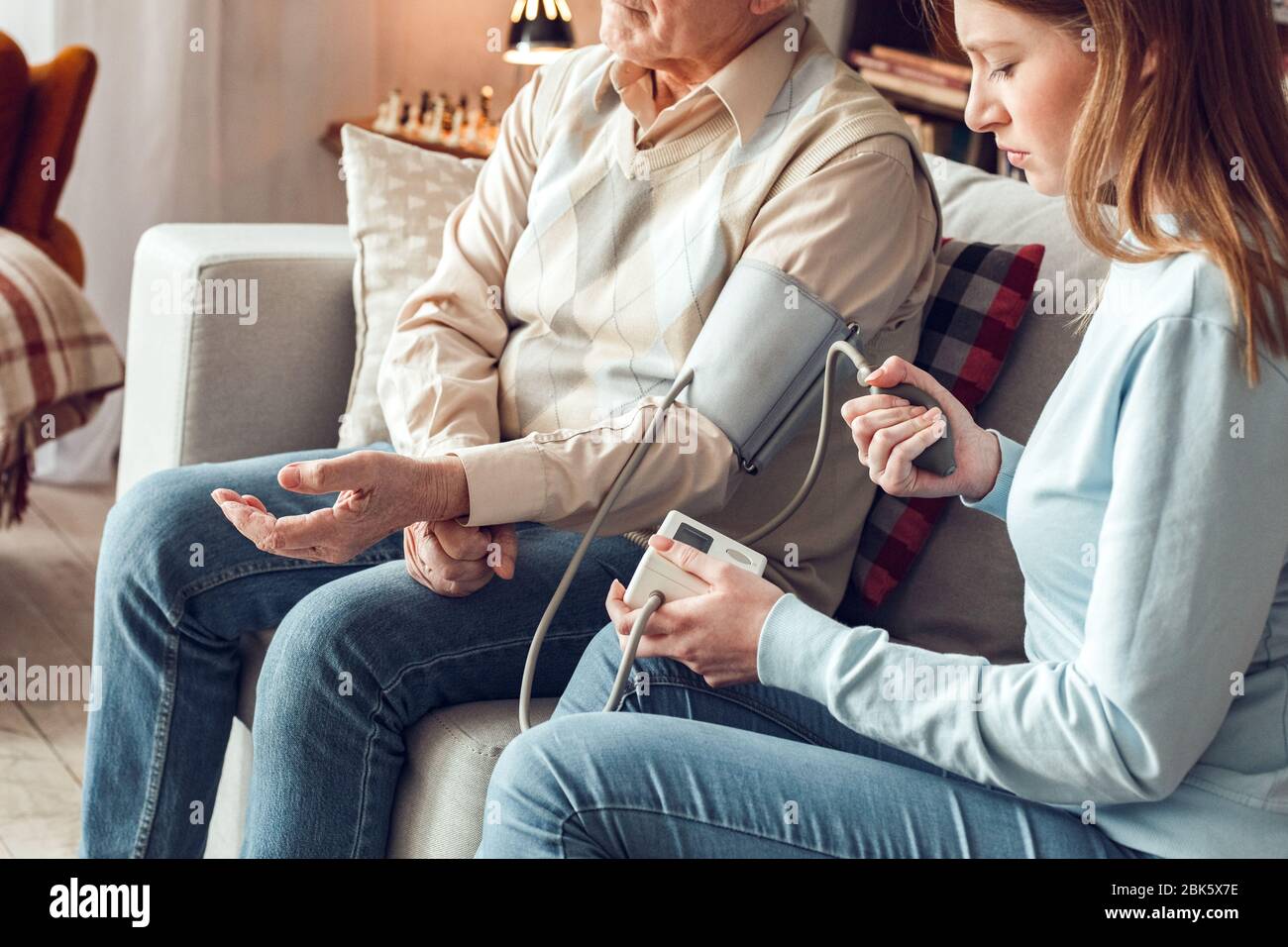 Vater und Tochter zu Hause Bibliothek sitzende Frau hilft Vater, Blutdruck zu messen Stockfoto