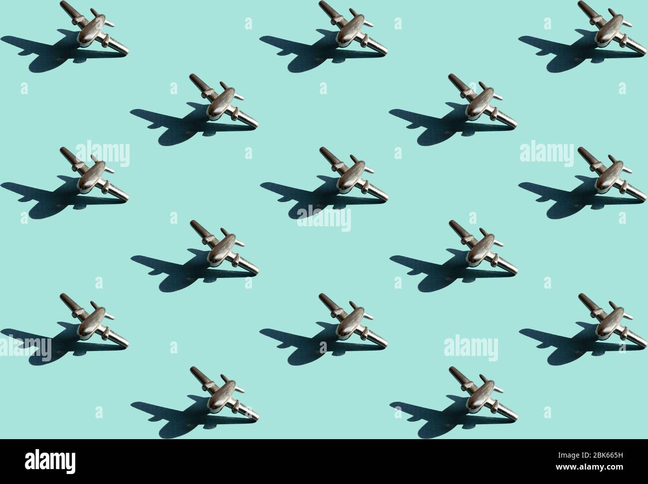 Fünfzehn Metallfiguren von kleinen Flugzeugen mit Schatten mit dem gleichen Abstand zwischen ihnen auf dem hellen mintfarbenen Hintergrund. Konzeptuelle geometrische Kunst tr Stockfoto