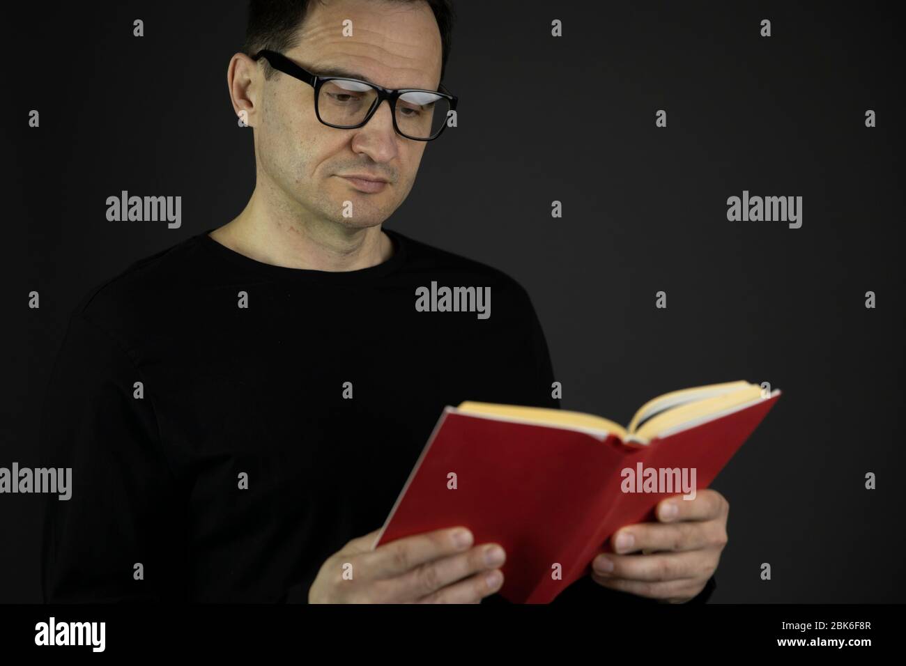 Schöner lässig gekleideter 40er Mann mit dunklen Haaren in Gläsern liest dicht rotes Buch Stockfoto